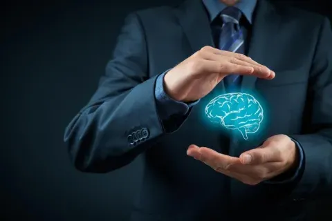 Persona protegiendo entre sus manos un cerebro luminoso, símbolo de la propiedad intelectual e industrial